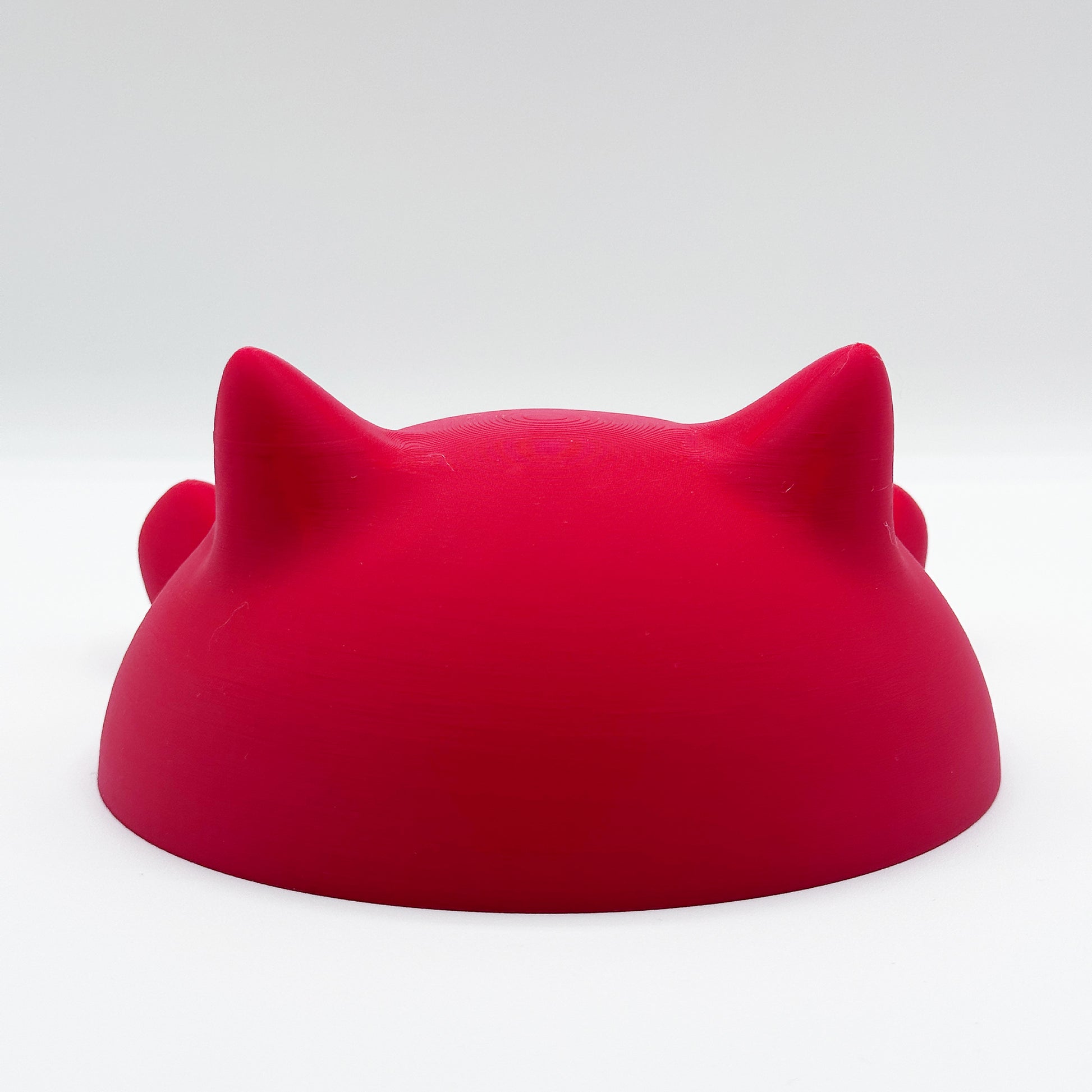 A red, rounded object with two pointed protrusions resembling cat ears on a white background. The shape suggests it could be the Blob Cat Desk Decor by Highly Obtainable.