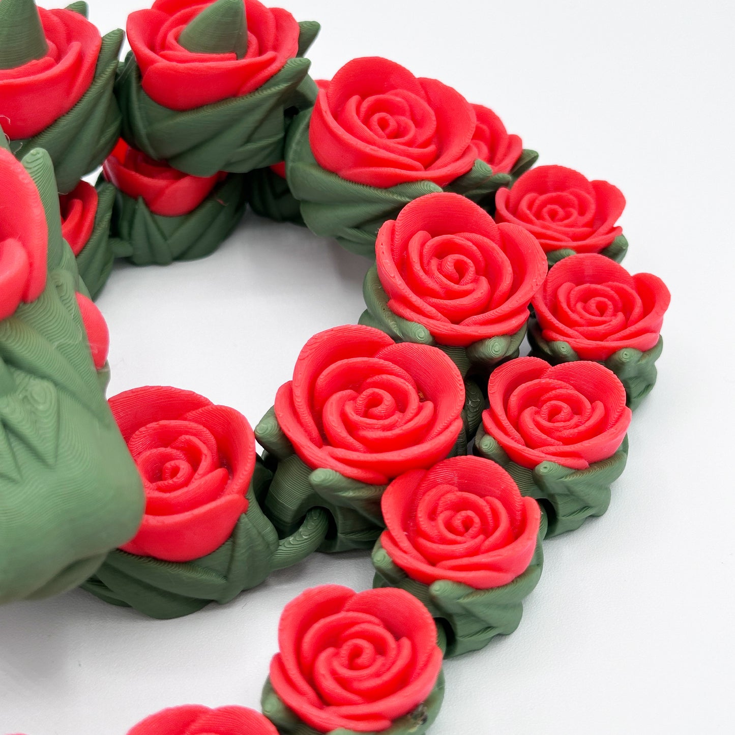 A close-up image of intricately designed, red spiral roses with green stems, appearing to be crafted from a smooth, glossy material. The dense arrangement, measuring 27 inches in product size, features roses aligned closely together against a white background. This is the Cinder Wing Rose Snake Dragon by Highly Obtainable.