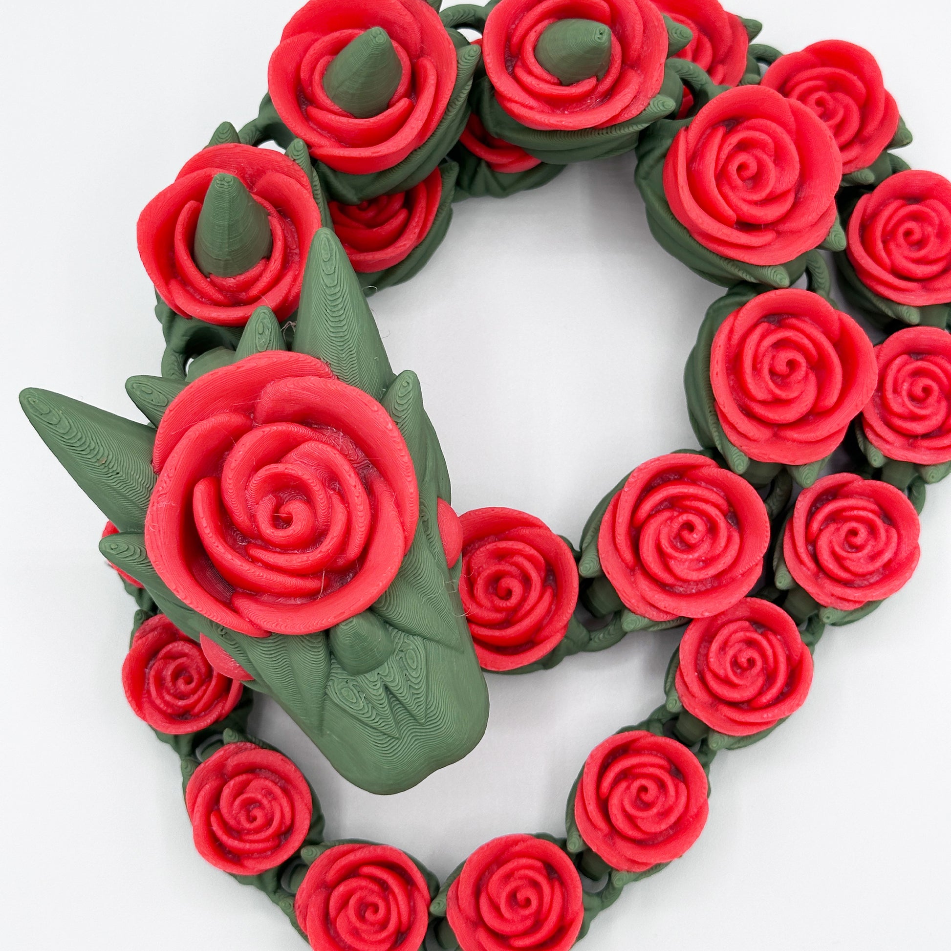 A Cinder Wing Rose Snake Dragon by Highly Obtainable made of red, rose-shaped beads intricately arranged on a green band. The design features a prominent rose at the center, with smaller roses surrounding it, forming a visually striking floral accessory. The product size is 27 inches, adding to its elegant dimensions.