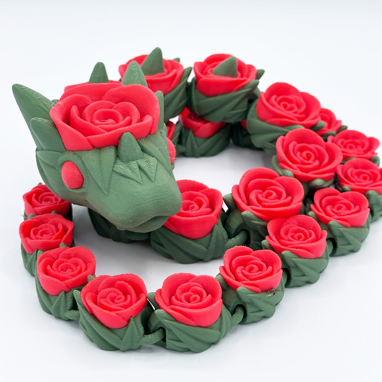 A 3D-printed Cinder Wing Rose Snake Dragon figure by Highly Obtainable, covered in red roses. Measuring 27 inches, the dragon is primarily green and strategically intertwined with intricately detailed roses along its body, enhancing its mythical appearance. The overall aesthetic is a blend of fantasy and floral elements.