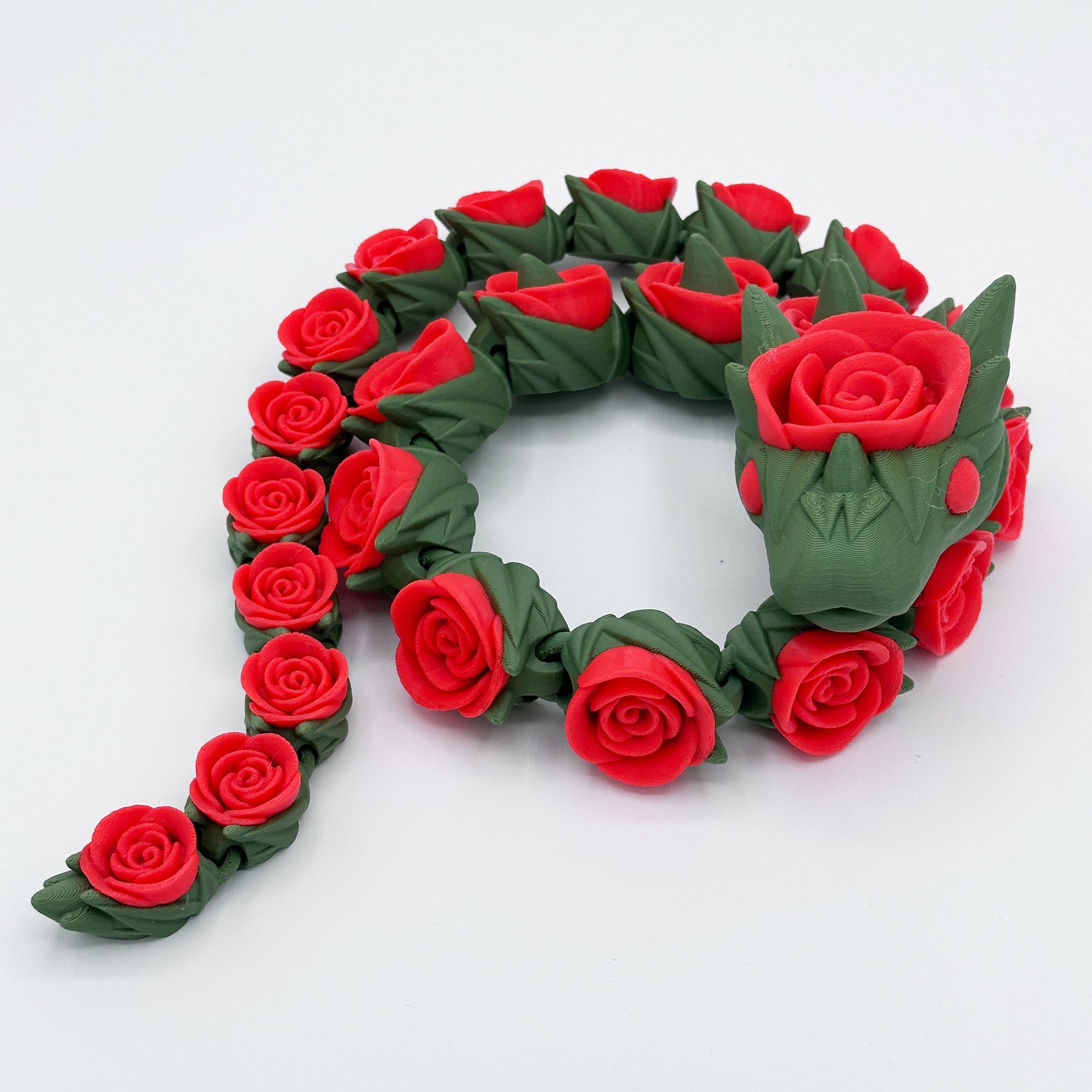 A **Highly Obtainable Cinder Wing Rose Snake Dragon** made entirely of red roses with green leaves. The dragon's body is a series of individually crafted roses, and its head features a rose as well, with detailed green facial features and a crown-like structure. The product size is 27 inches in height, adding to its majestic presence.