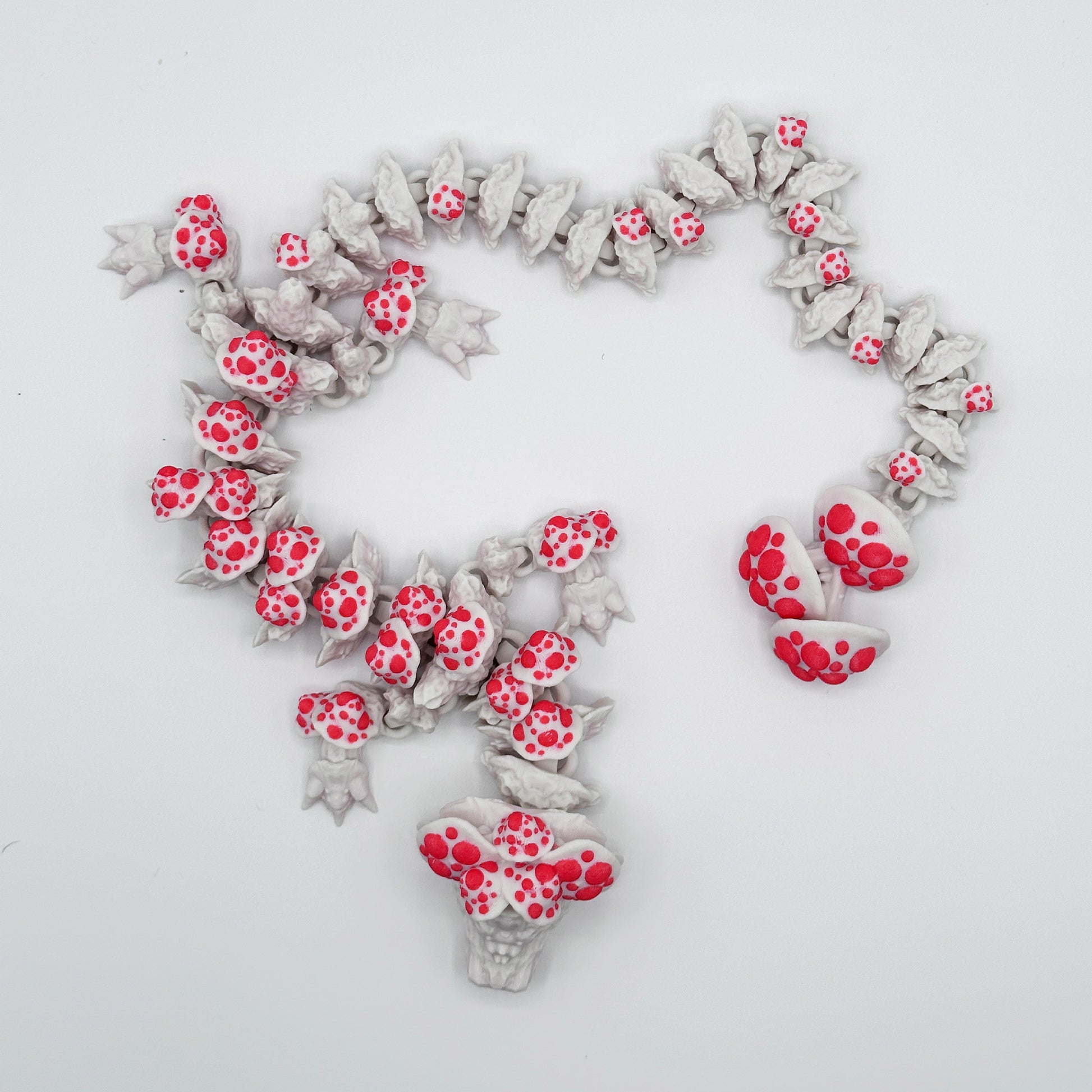 A series of white ceramic Cinder Wing Mushroom Dragons, adorned with red polka dots, are arranged in a spiral pattern on a white background. Like a sensory figurine, several clusters of polka-dotted dragons form denser groups within the spiral, creating a textured visual effect.