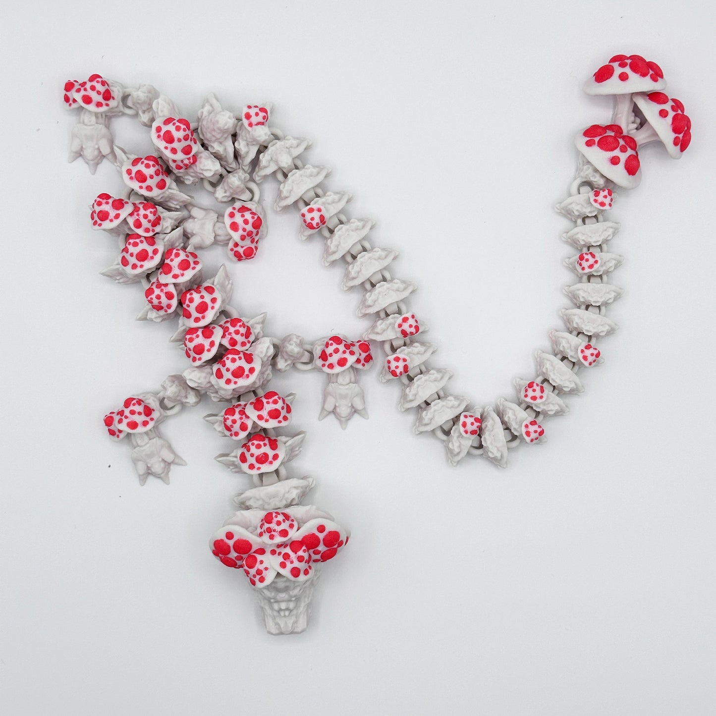 A Cinder Wing Mushroom Dragon by Highly Obtainable, crafted from sustainable PLA. The design features multiple small skulls along the chain and a larger skull at the center, with clusters of red-spotted mushrooms adding a vibrant contrast.